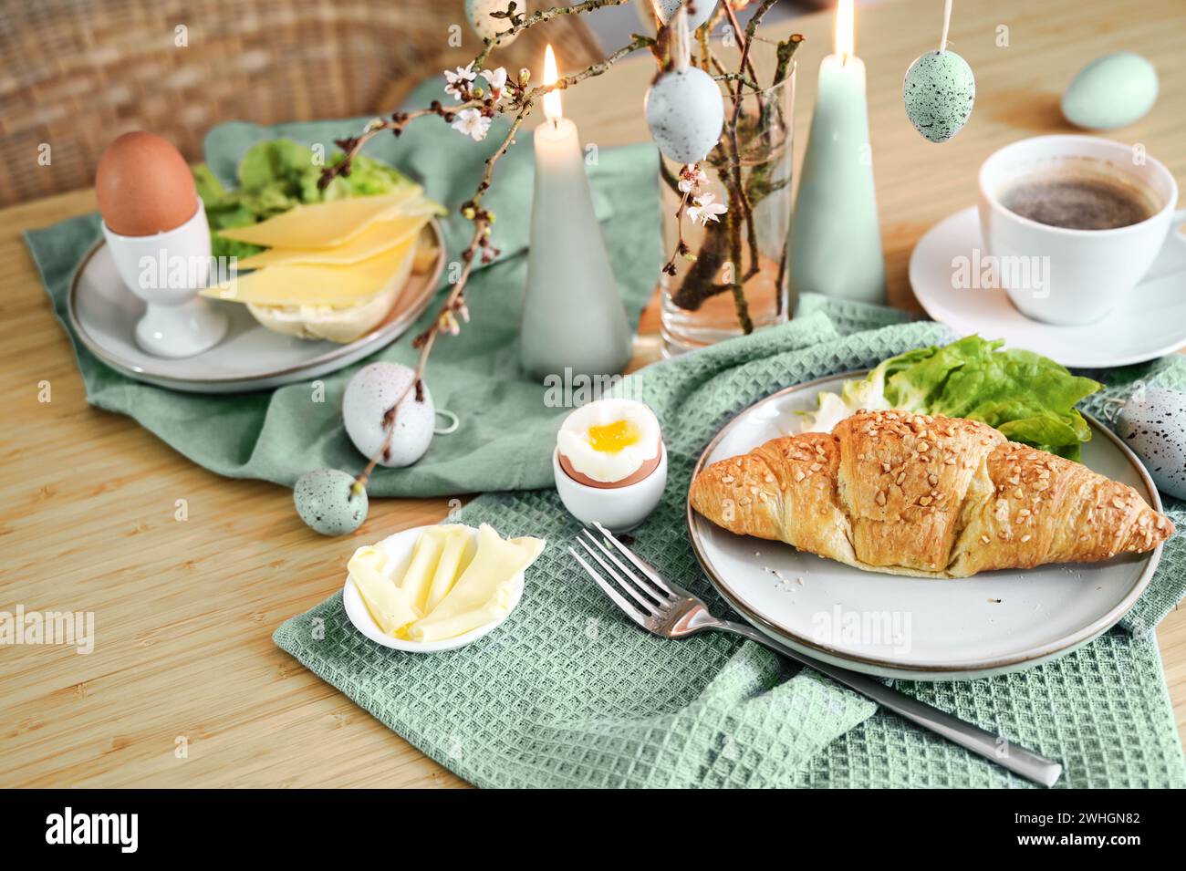 Colazione con uova di Pasqua, croissant, caffè e decorazione verde salvia con candele su un tavolo di legno, spazio per le copie, foc selezionati Foto Stock