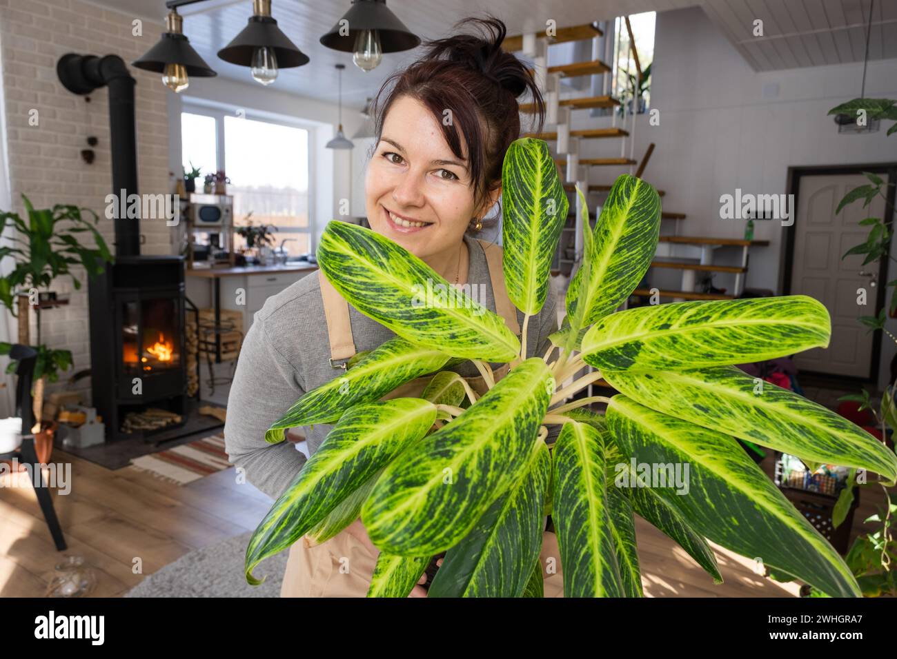Una donna felice in una casa verde con una pianta in vaso nelle sue mani sorride, si prende cura di un fiore. L'interno di un accogliente eco-frien Foto Stock
