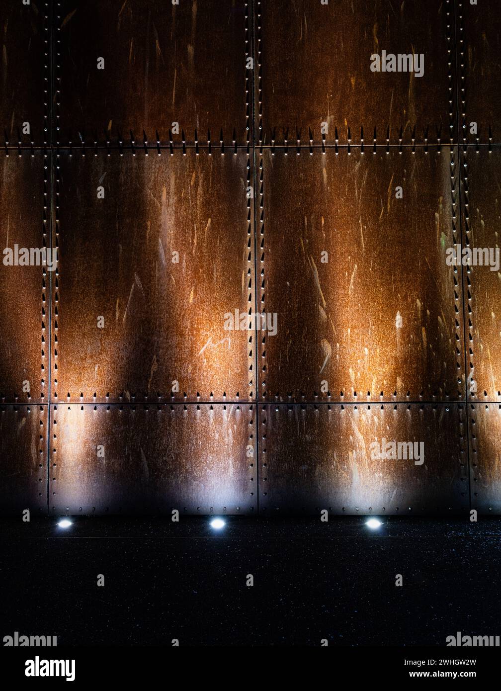 Una parete industriale in metallo arrugginito illuminata da lampade luminose Foto Stock