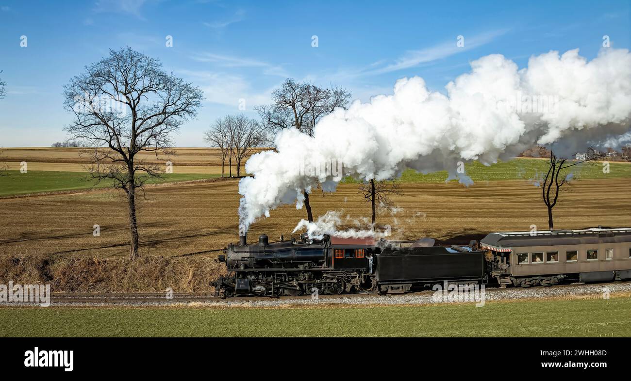 Drone Vista di una locomotiva a vapore in avvicinamento a carrozze passeggeri trainate, soffia fumo bianco Foto Stock