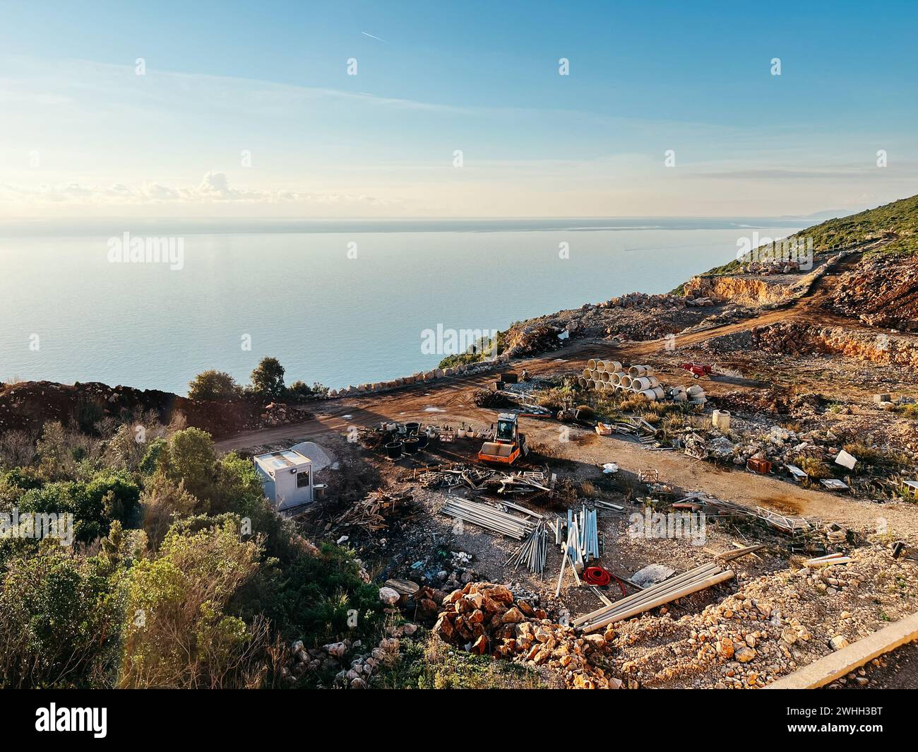 Il trattore si trova in un cantiere con materiali da costruzione su una collina vicino al mare Foto Stock