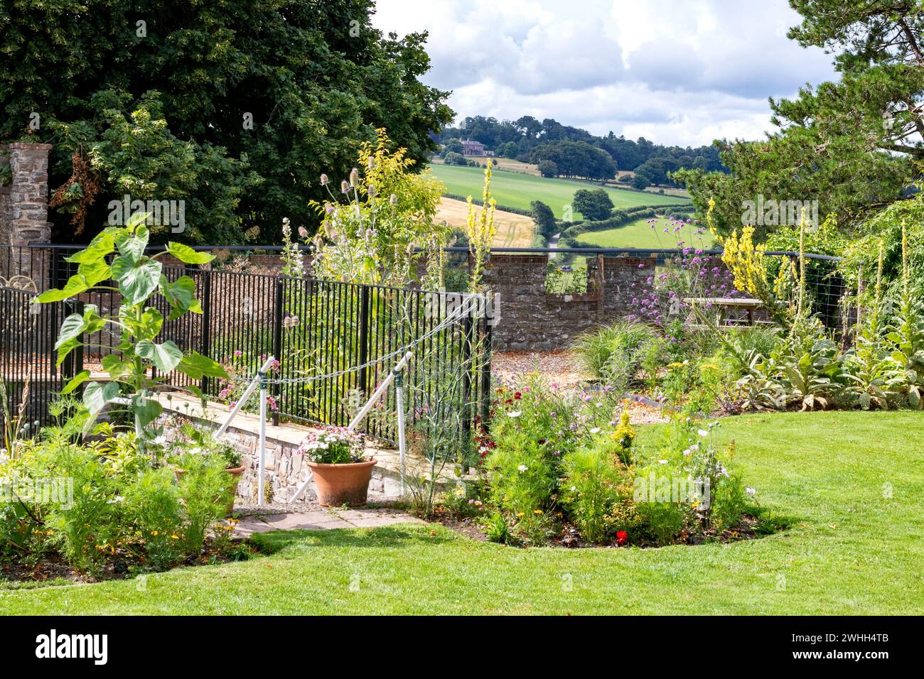 Tranquillo giardino nei giardini comunitari del grande castello di Torrington con muro di confine, ringhiere, scalini e alberi su Castle Hill, con vista rurale. Foto Stock