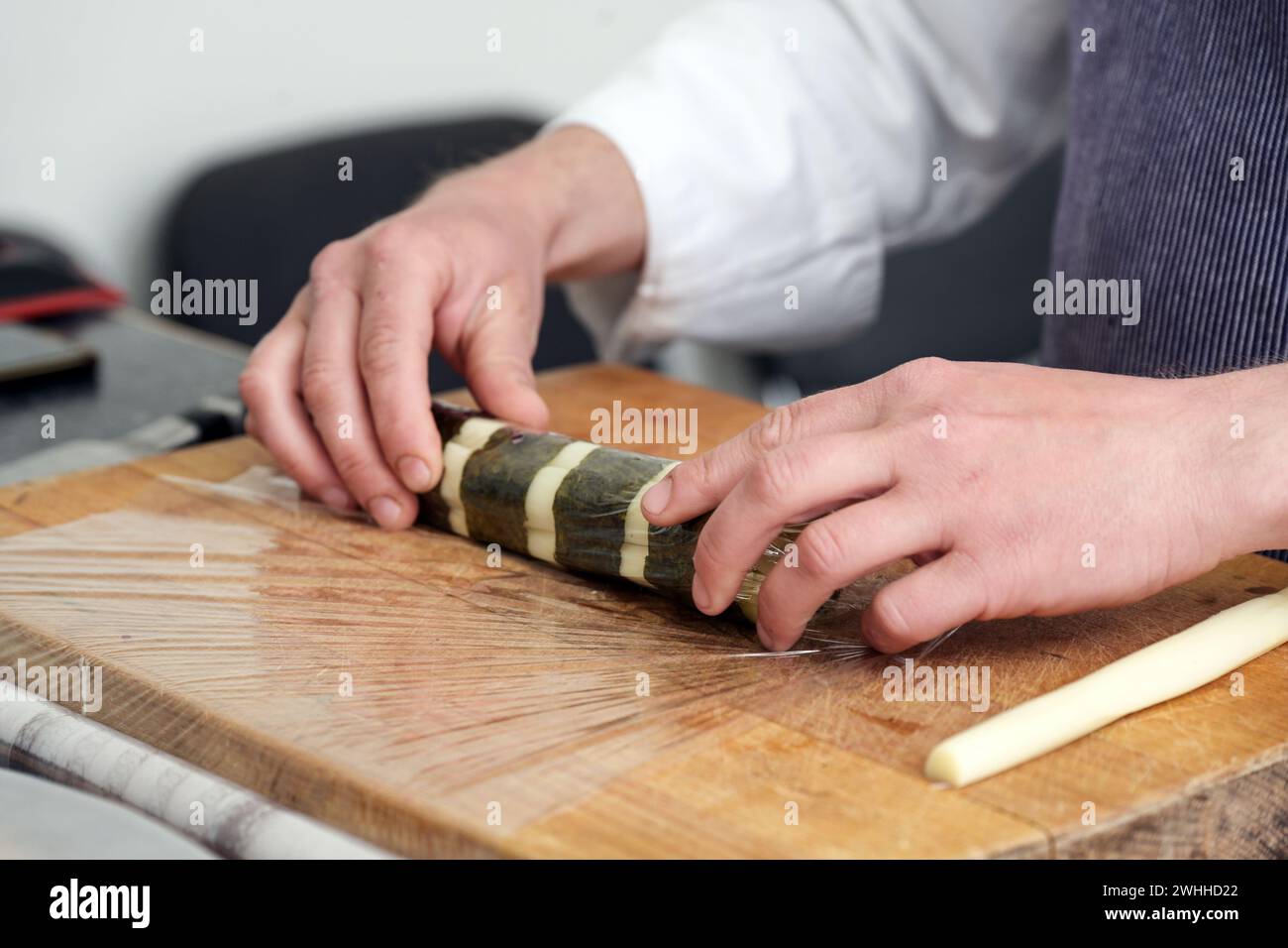Mani di uno chef che arrotola asparagi bianchi in foglie di alghe nori su un tavolo da cucina, preparando la cucina per un gourmet vegetariano Foto Stock