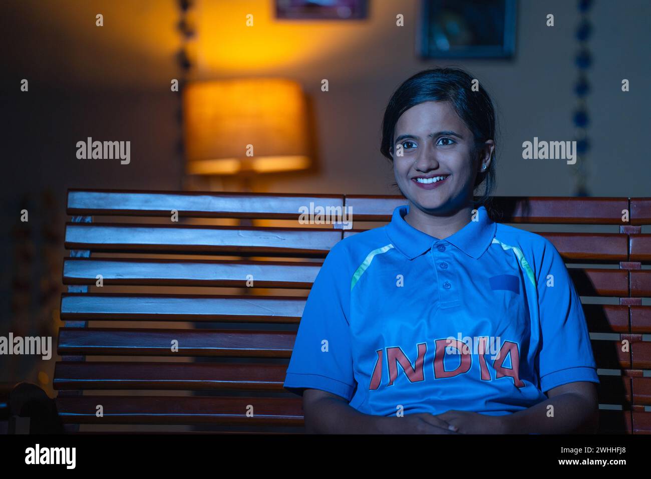 Curios giovane ragazza in maglia indiana che guarda la partita di cricket in tv o in televisione a casa - concetto di tifosa, coppa del mondo e campionato. Foto Stock
