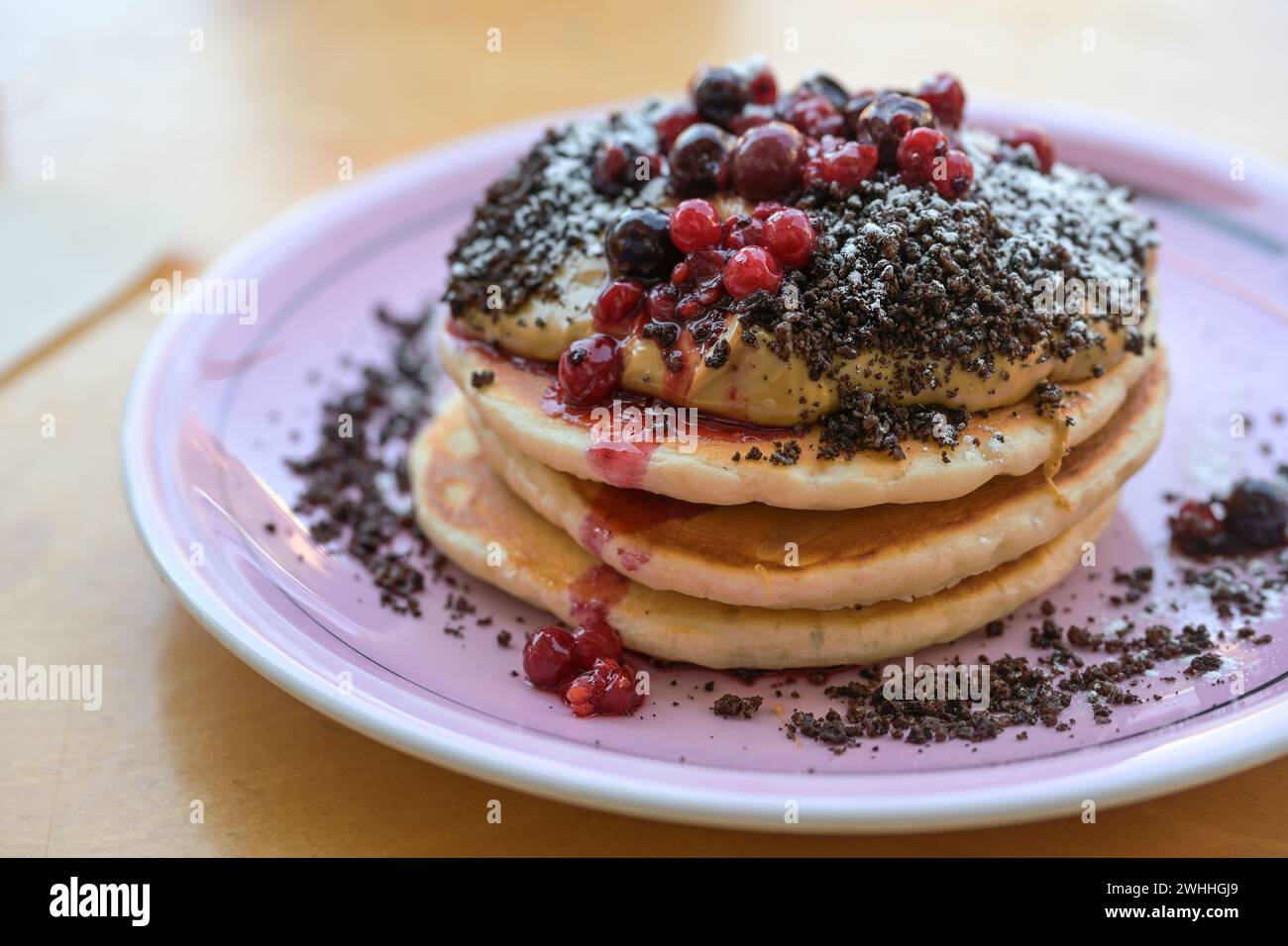 Pancake impilati con crema al burro di arachidi, frutti di bosco, crumble e zucchero a velo su un piatto, colazione dolce, brunch o piatto da dessert, Foto Stock