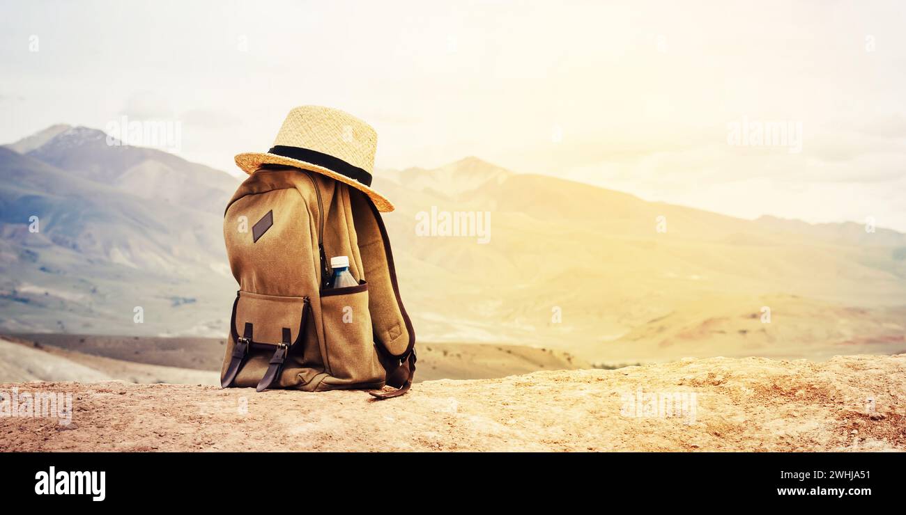 Zaino beige, bottiglia d'acqua e cappello di paglia sulla collina in montagna. Concetto di viaggio attivo. Tonificante il tramonto Foto Stock