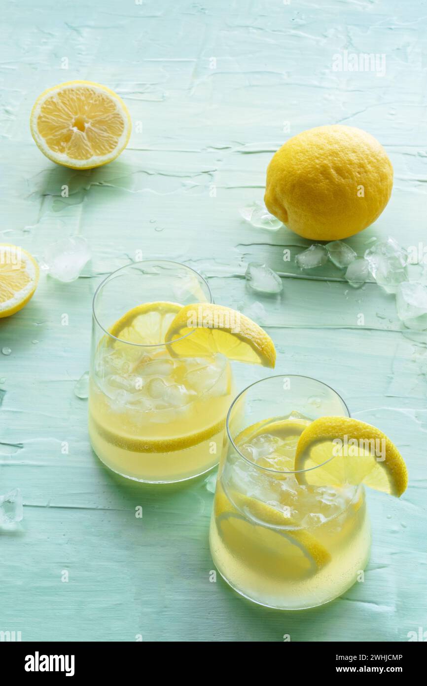 Limonata. Bere acqua di limone con ghiaccio, due bicchieri e frutta su blu Foto Stock