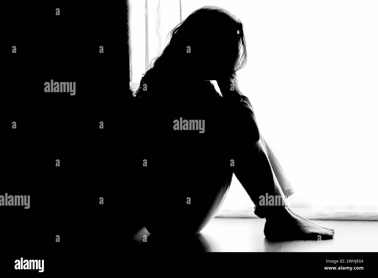 Signora mature infelice, donna in silhouette, seduta sul pavimento con la schiena illuminata. Pensieri deprimenti. Foto Stock