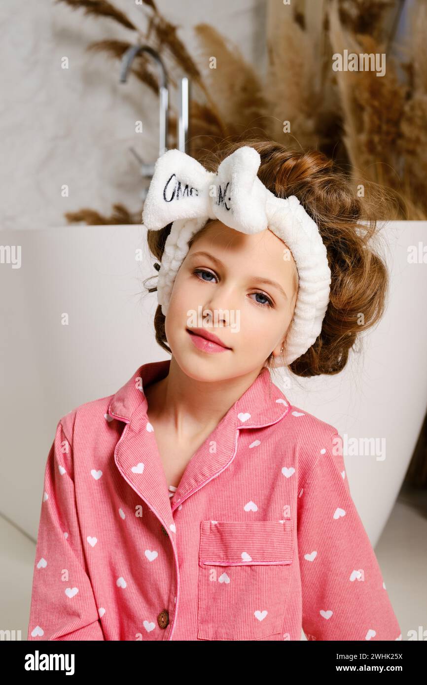 Ritratto di una bambina di nove anni in pigiama rosa e una fascia per capelli che supporta capelli lunghi e spessi Foto Stock