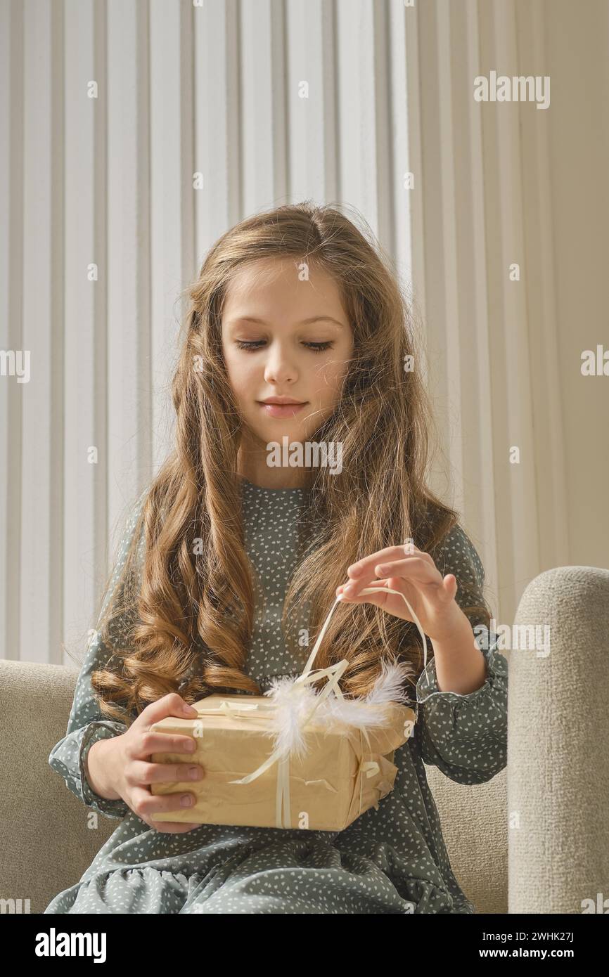 Ritratto di una ragazza in un abito di menta, seduta su una sedia e tirando il nastro della confezione regalo Foto Stock