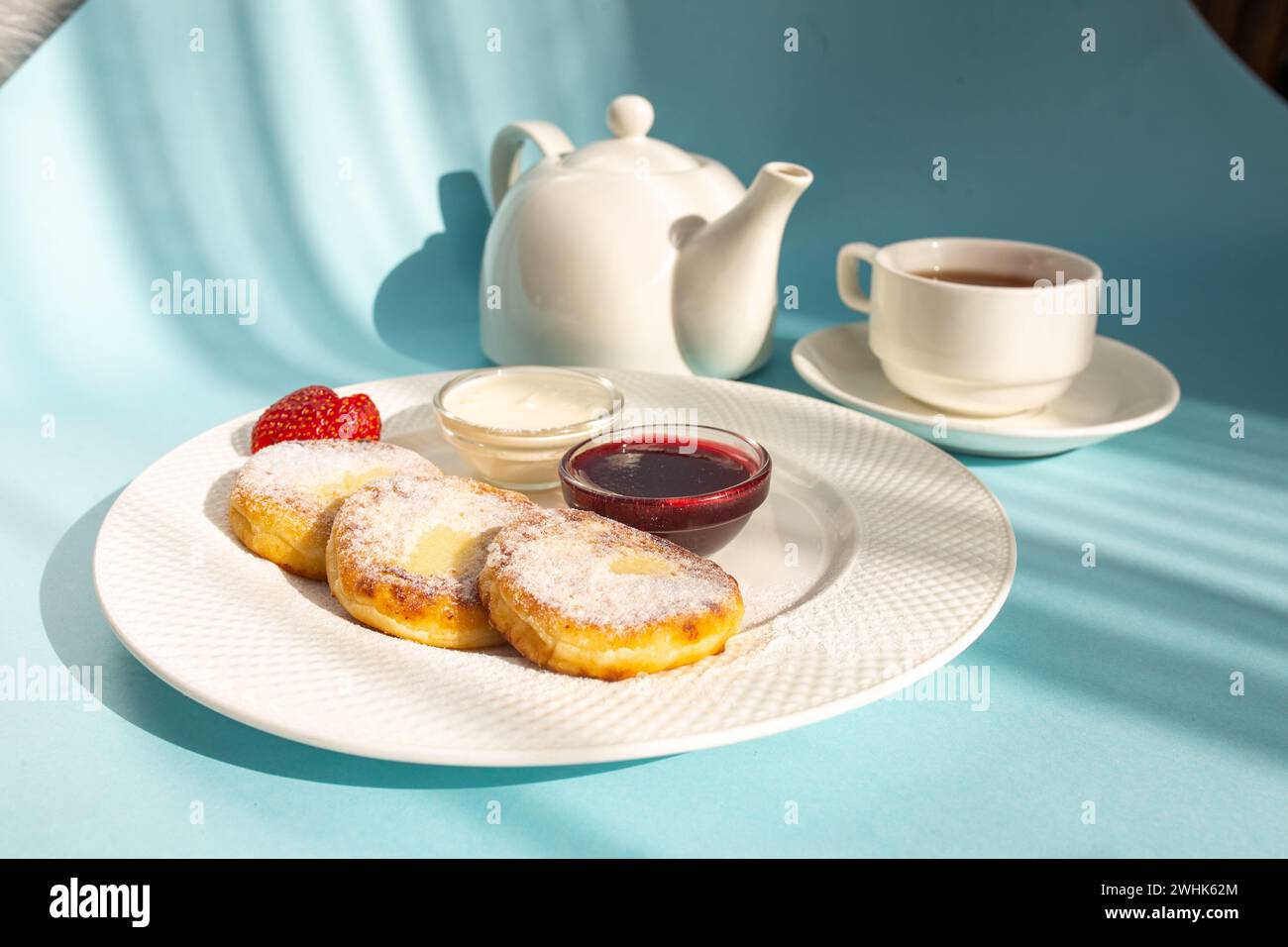 Gusta una sana colazione con soffici pancake al formaggio conditi con marmellata, fragole fresche e un cucchiaio di panna acida. Dai energia alla tua giornata Foto Stock