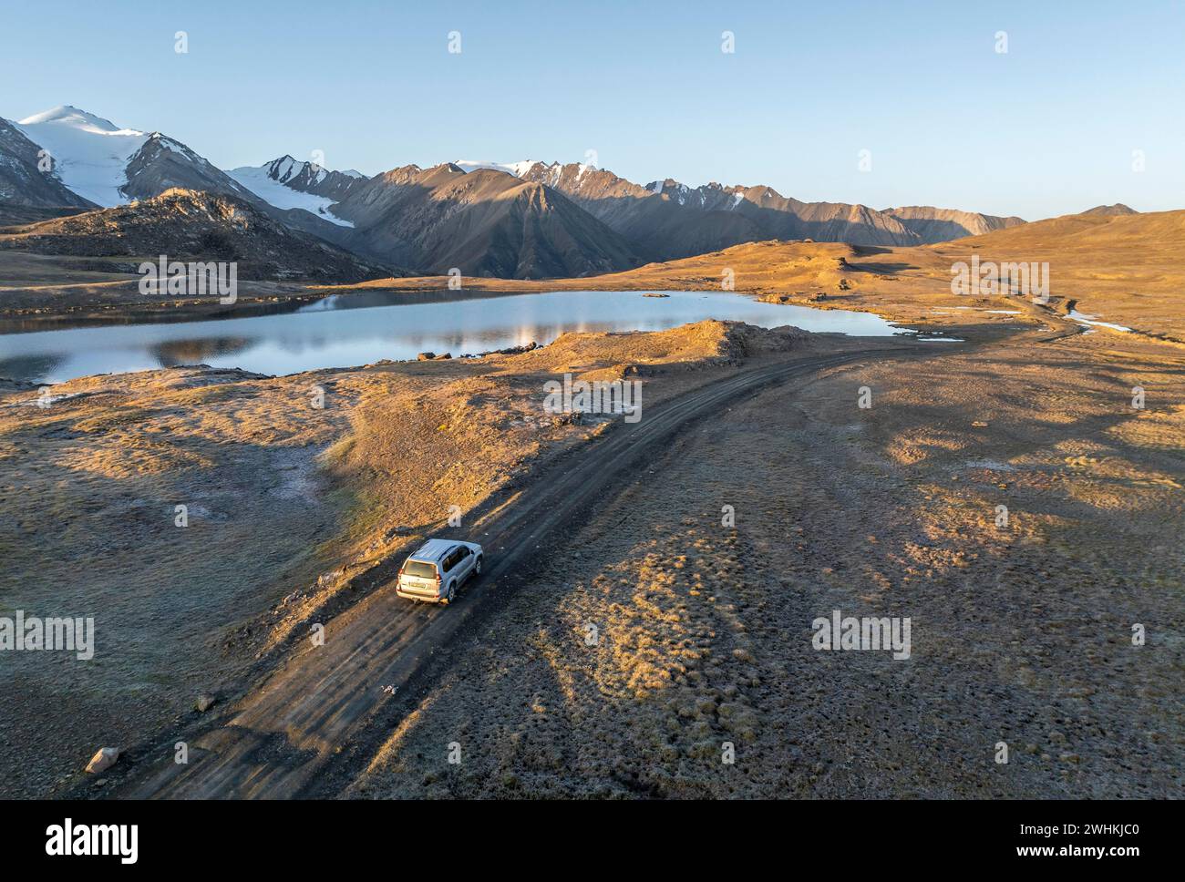 Vista aerea, veicolo fuoristrada su pista di ghiaia, picco di montagna e lago di montagna, atmosfera serale, lago Arabel al passo Arabel, provincia di Issyk Kul Foto Stock
