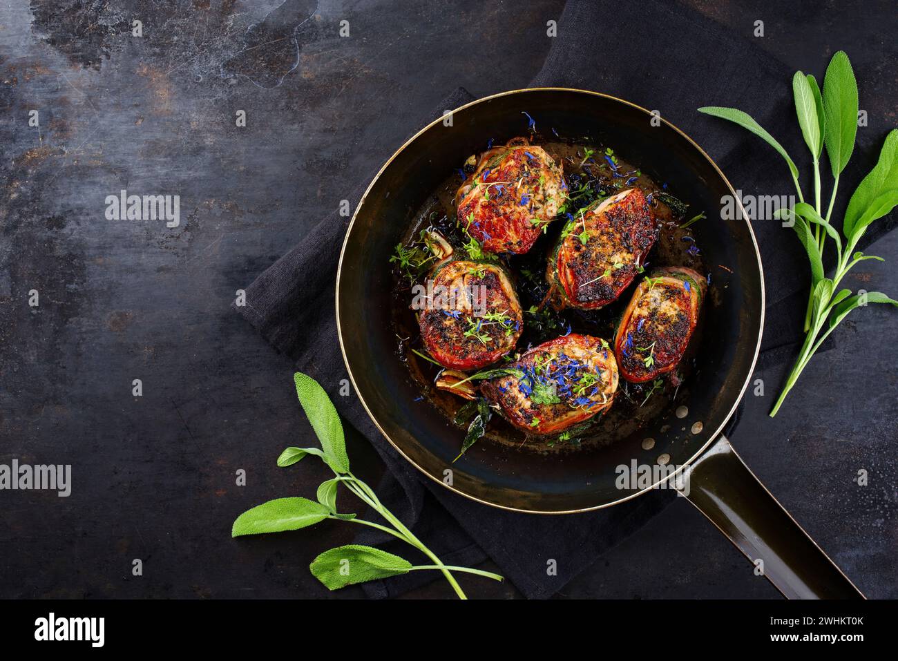 Tradizionali medaglioni di filetto di vitello arrosto con rivestimento di pancetta e foglie di salvia in salsa di burro serviti come vista dall'alto su un battuto rustico Foto Stock