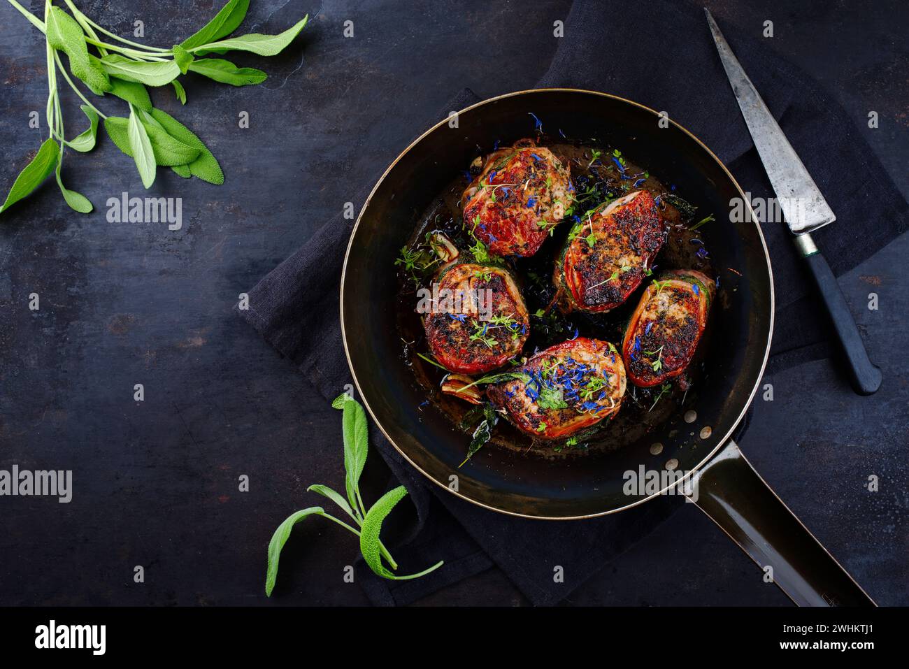 Tradizionali medaglioni di filetto di vitello arrosto con rivestimento di pancetta e foglie di salvia in salsa di burro serviti come vista dall'alto su un battuto rustico Foto Stock