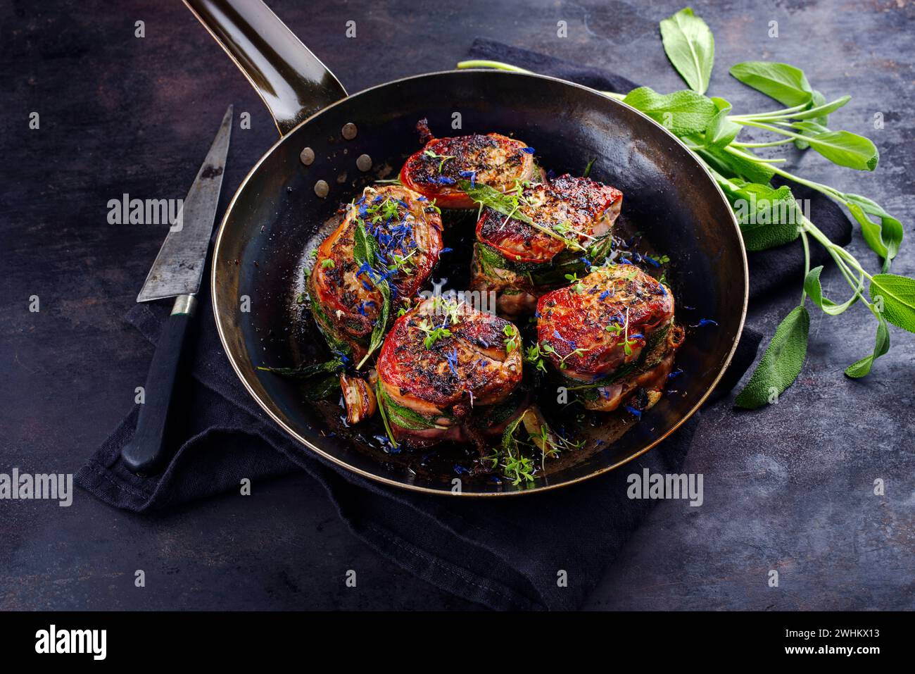 Tradizionali medaglioni di filetto di vitello arrosto con rivestimento di pancetta e foglie di salvia in salsa di burro serviti da vicino su un battuto rustico Foto Stock