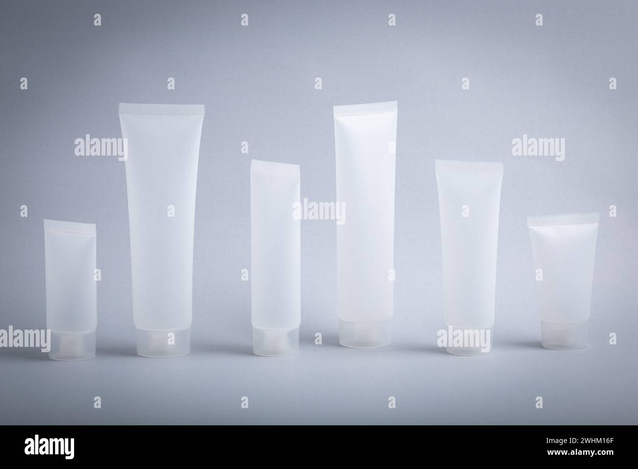 Set di provette cosmetiche vuote bianche opache con sfondo grigio semplice e pulito, concetto di cosmetologia, corpo e pelle Foto Stock