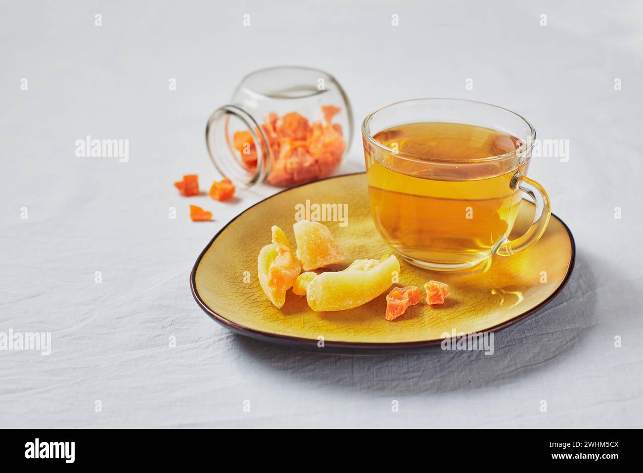 Delizioso tè nero in bicchiere e frutta candita su piattino giallo Foto Stock