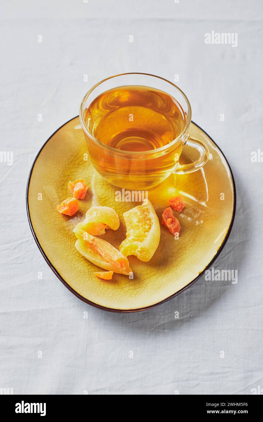 Delizioso tè nero in bicchiere e frutta candita su piattino giallo Foto Stock