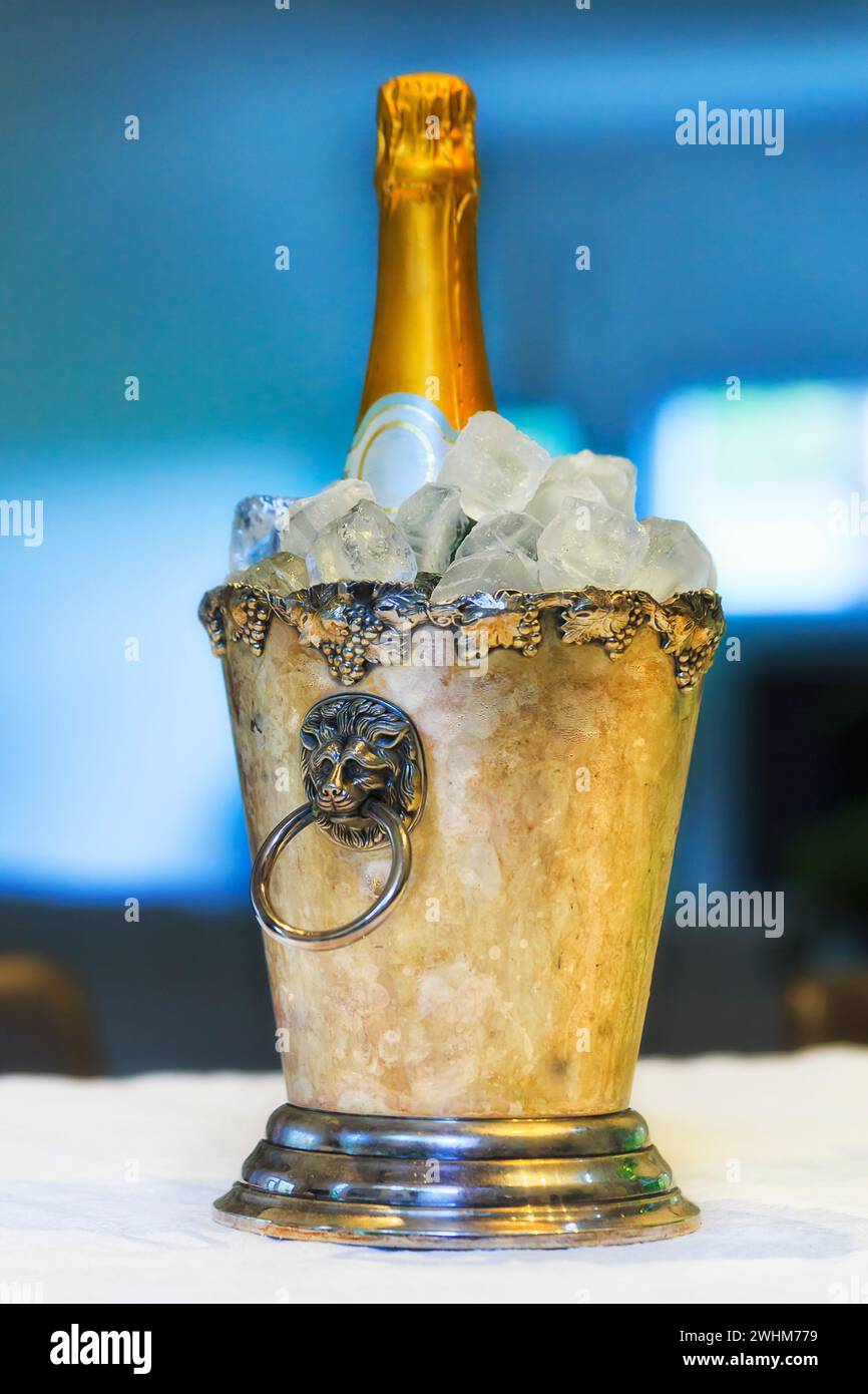 Bottiglia di champagne con tappo frizzante in un secchio di ghiaccio servito su un tavolo da pranzo. Foto Stock