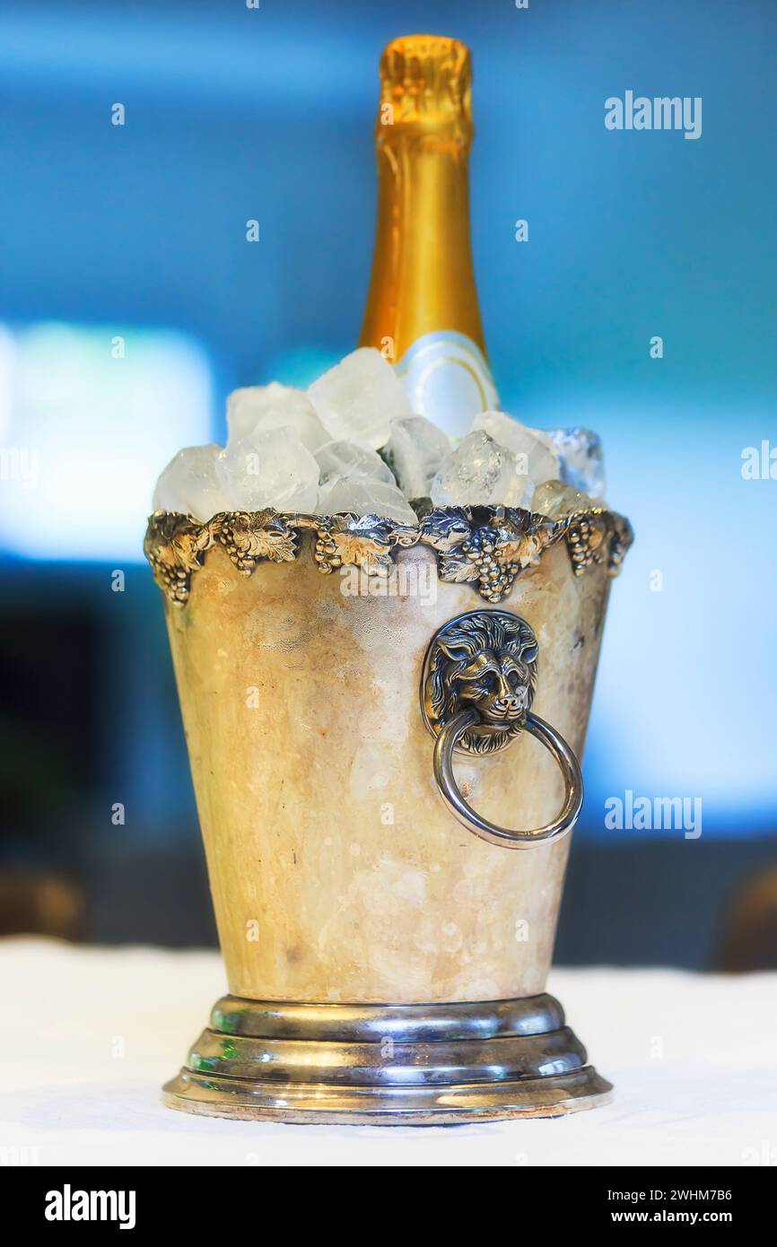 Bottiglia di vino frizzante bianco in secchio di ghiaccio su un tovagliolo bianco - celebrazione e stile di vita natura morta. Foto Stock