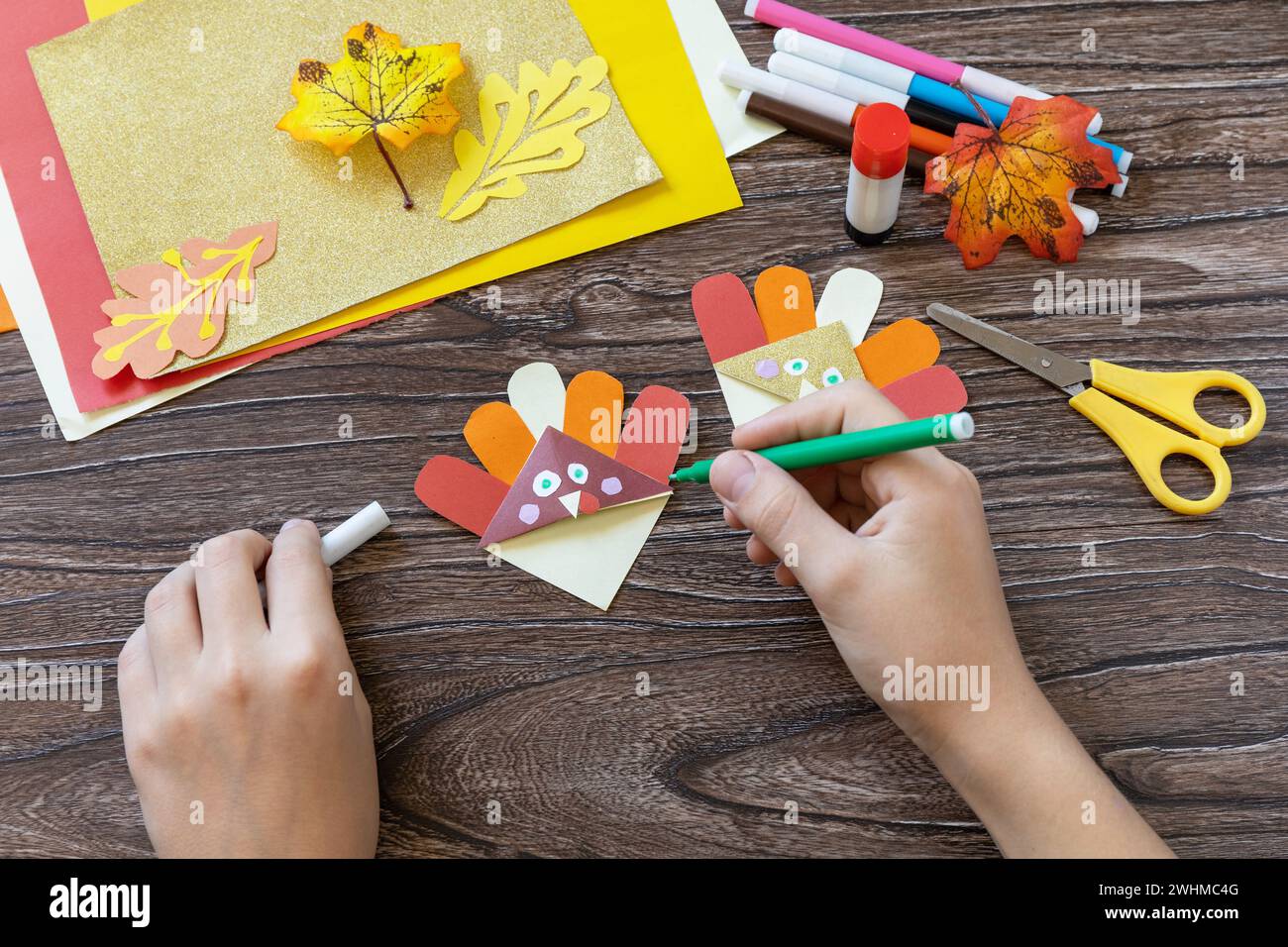 Fase 12 delle istruzioni. Carta di tacchino segnalibro artigianale del giorno del Ringraziamento su un tavolo di legno. Progetto artistico per bambini, fatto a mano, artigianato per bambini Foto Stock