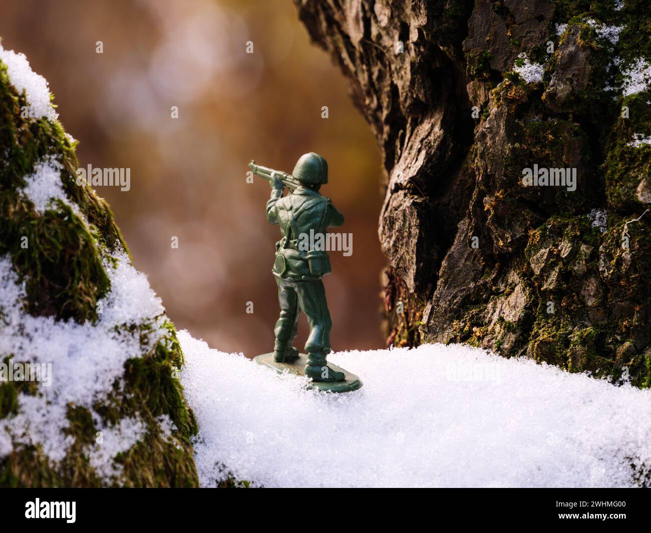 Un soldato giocattolo si staglia su un ramo marrone, verde muschio e innevato in inverno ghiacciato, freddo e gelido. Foto Stock