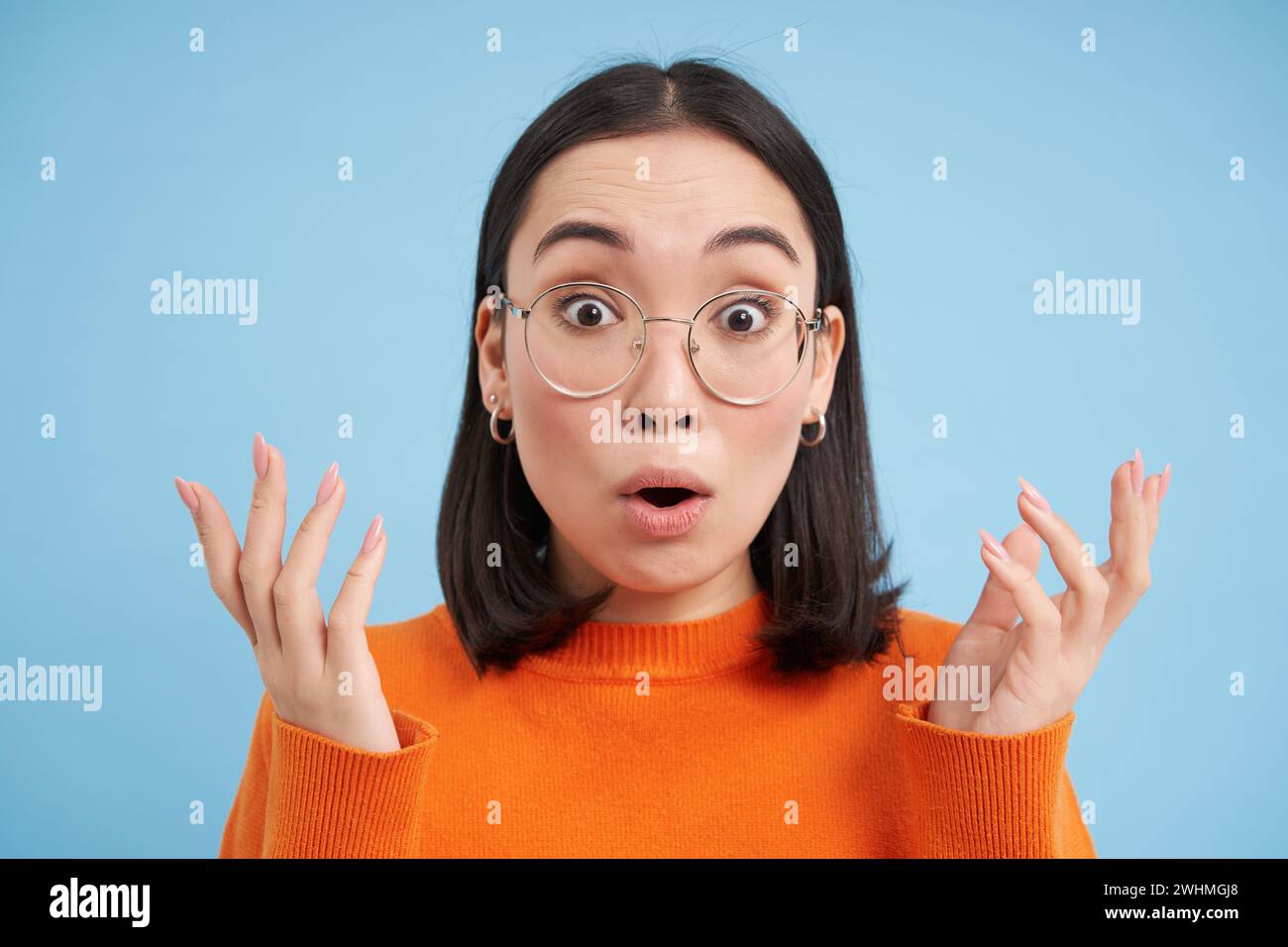 Occhiali e occhiali, concetto di ottica. Ritratto di bella donna asiatica in nuovi occhiali, sembra sorpreso, si erge su blu b Foto Stock