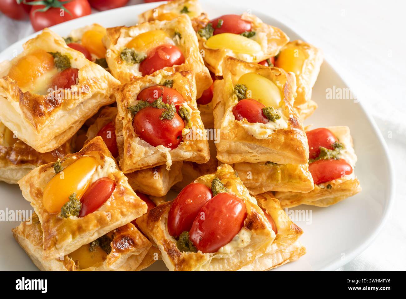 Stuzzichini con pasta sfoglia con pomodoro, formaggio spalmabile e pesto alle erbe, finger food su un piatto bianco per una festa fredda a buffet, focu selezionata Foto Stock