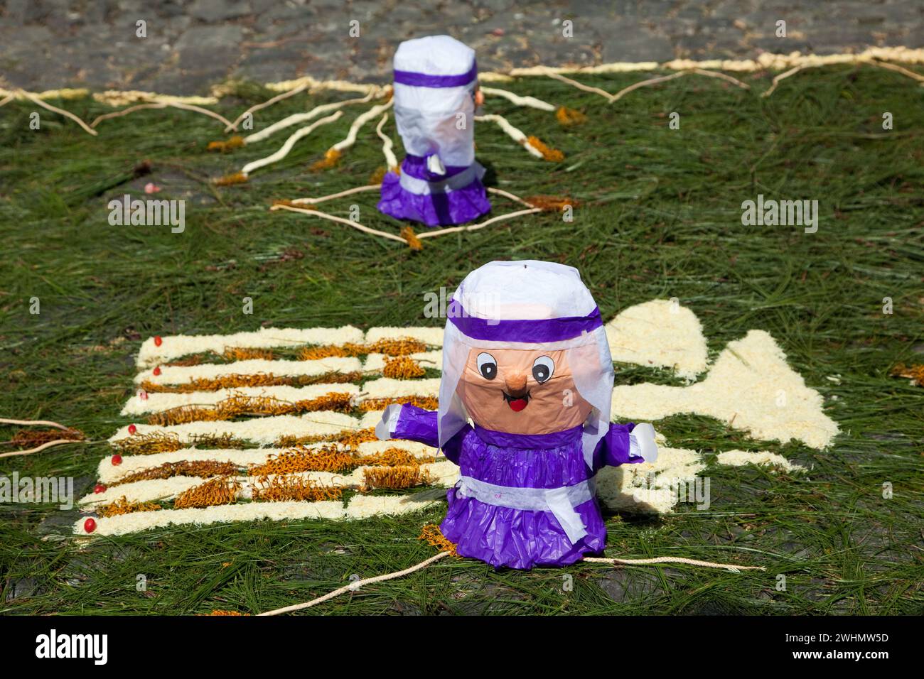 Antigua, Guatemala. Le bambole Cucuruchos decorano un alfombra (tappeto) di aghi di pino e altri materiali tradizionali in una strada prima dei pas Foto Stock