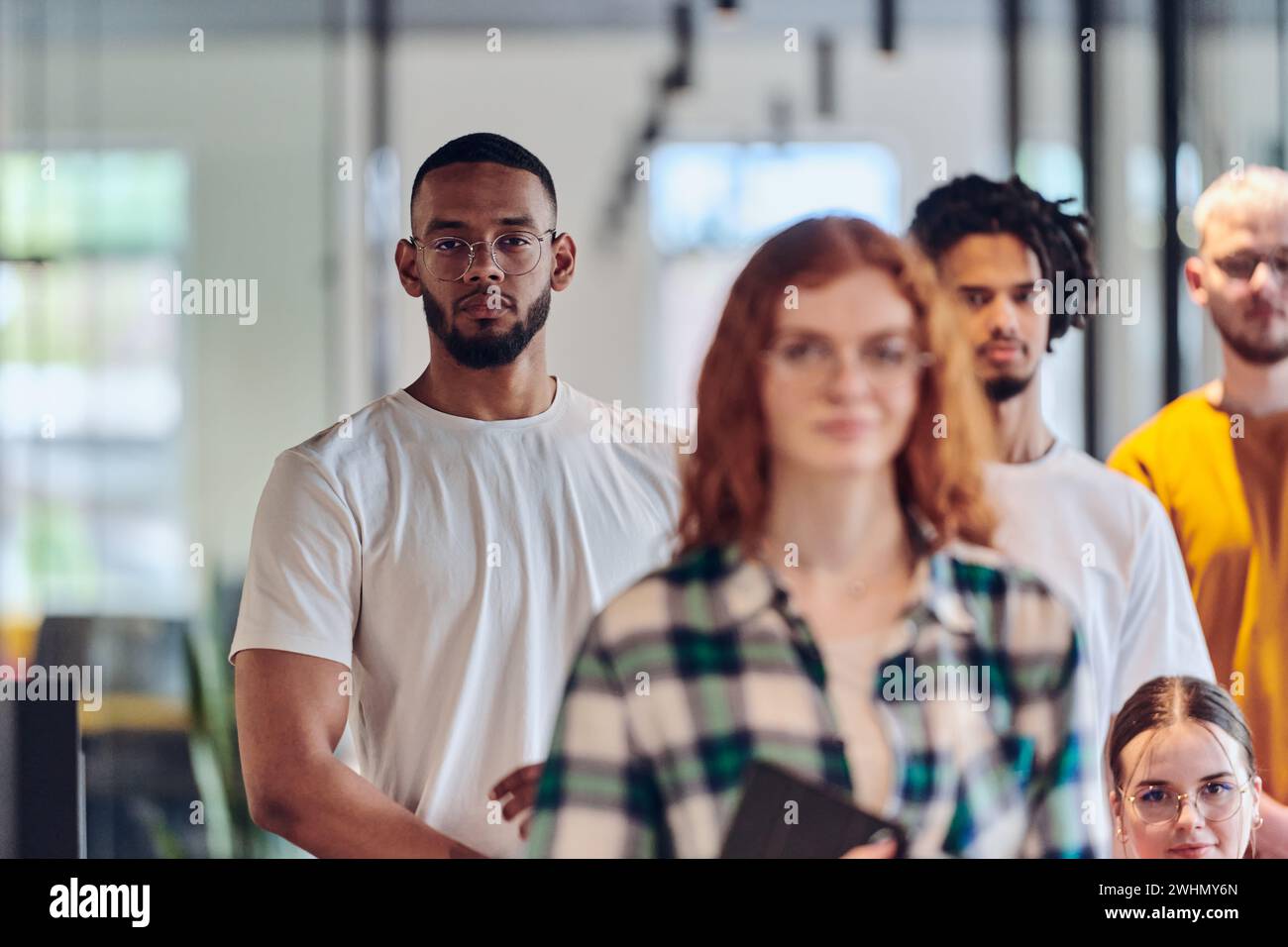 Un gruppo eterogeneo di uomini d'affari che camminano per un corridoio nell'ufficio chiuso in vetro di una startup moderna, inclusa una persona in una Foto Stock