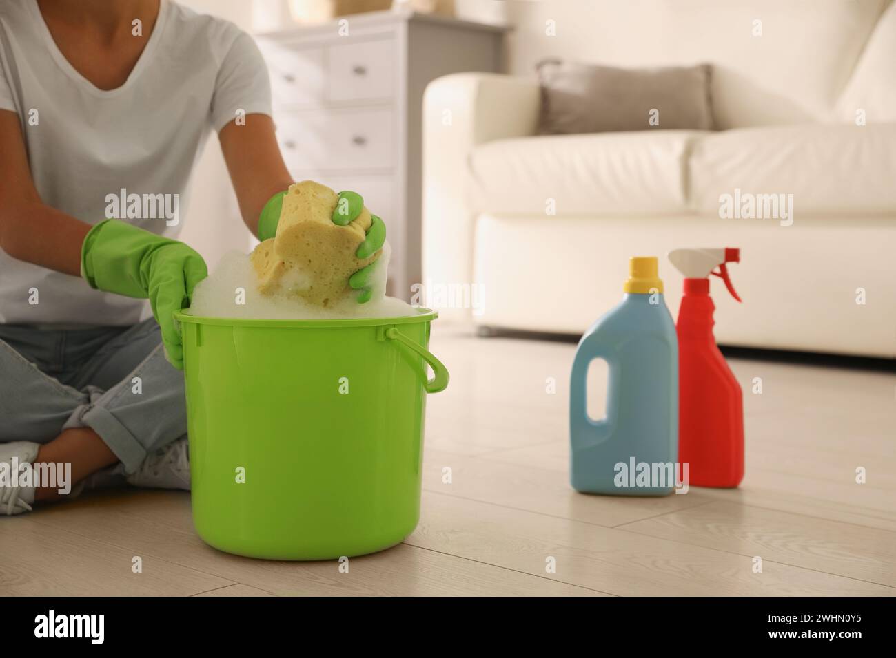 Donna che tiene spugna con schiuma sopra secchio interno, primo piano. Pulizia dei materiali di consumo Foto Stock