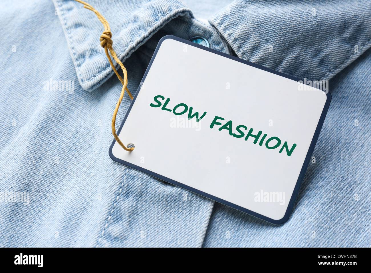 Consumo consapevole. Aggiungi un tag con le parole Slow Fashion su camicia in denim e primo piano Foto Stock