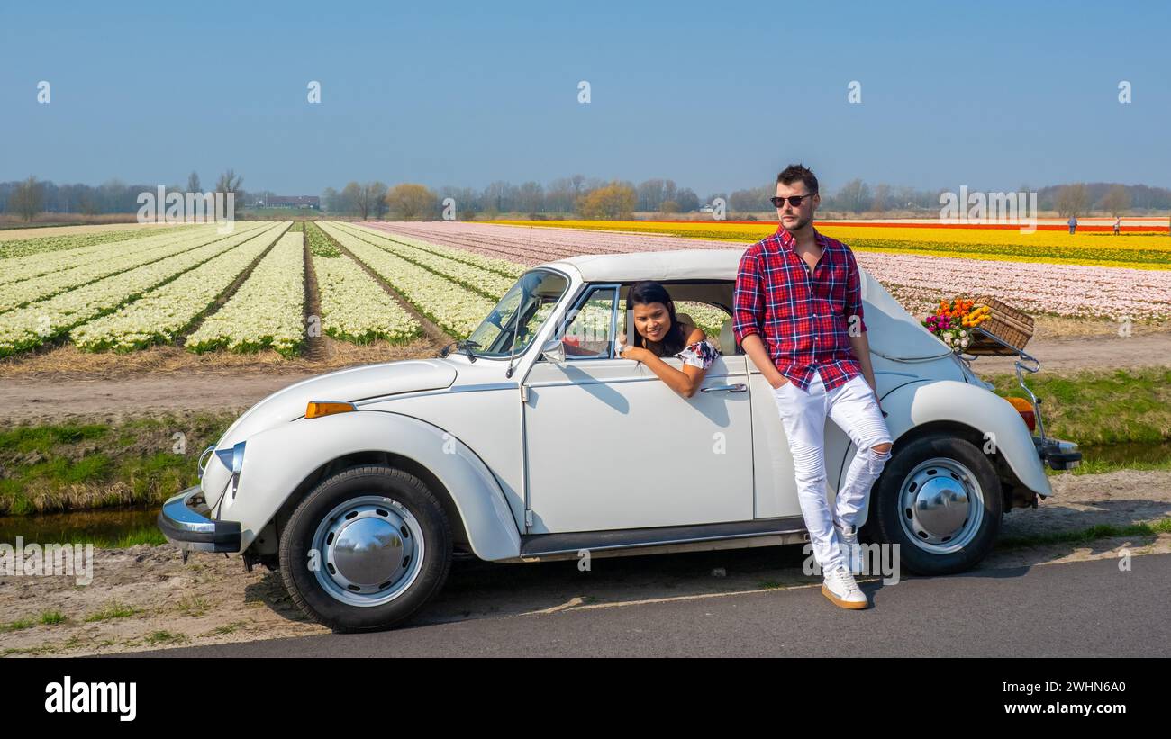 Coppia che fa un viaggio su strada con una vecchia auto d'epoca nella regione olandese dei fiori con campi di tulipani Foto Stock