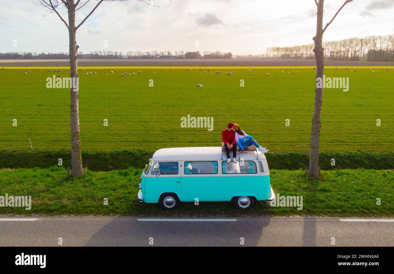 Coppia che fa un viaggio su strada con una vecchia auto d'epoca nella regione olandese dei fiori con campi di tulipani Foto Stock Coppia che fa un viaggio su strada con una vecchia auto d'epoca nella regione olandese dei fiori con campi di tulipani Foto Stock