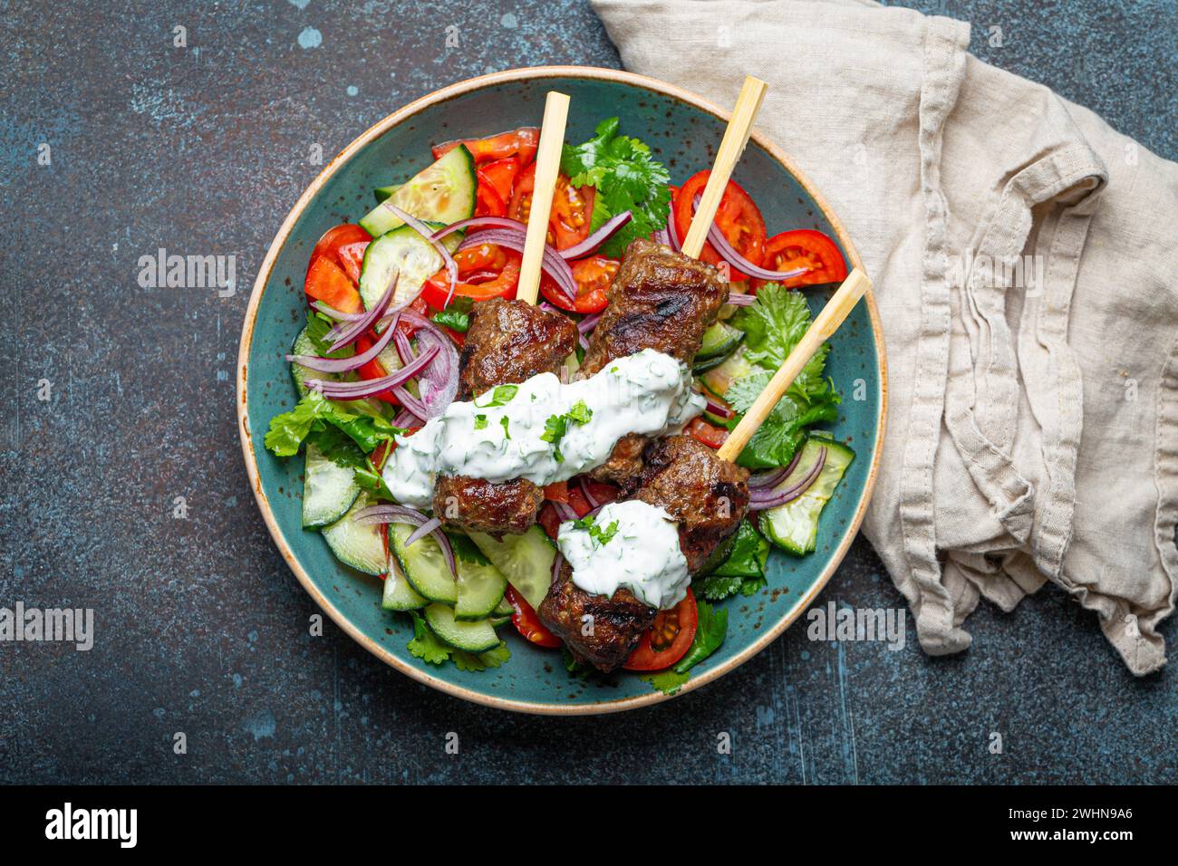 Spiedini grigliati di carne di manzo spiedini su bastoncini serviti con insalata di verdure fresche su piatto su sfondo rustico di cemento dall'alto. Foto Stock