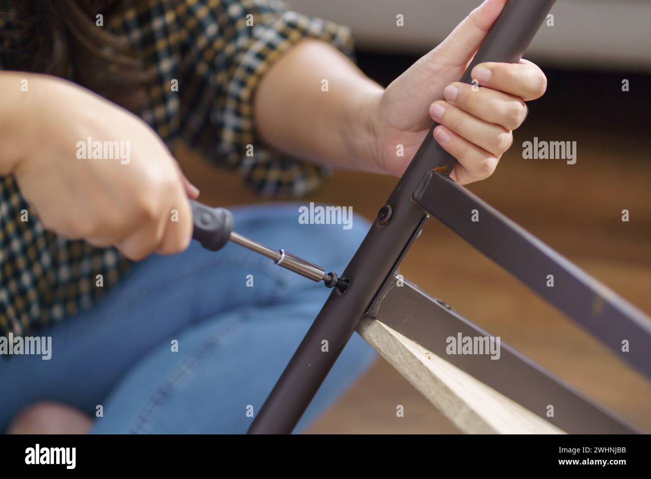La donna asiatica ripara autonomamente i mobili rinnovati utilizzando attrezzature per riparare i mobili da casa, seduti sul pavimento Foto Stock