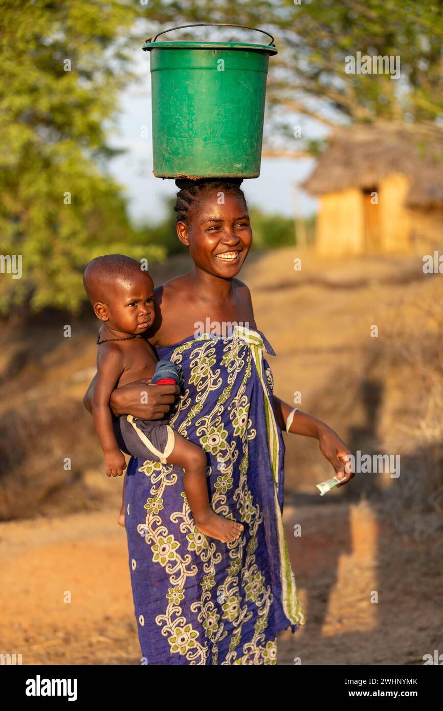 Donna con bambino in mano e contenitore in testa, una vista comune in questo villaggio rurale etiope Foto Stock