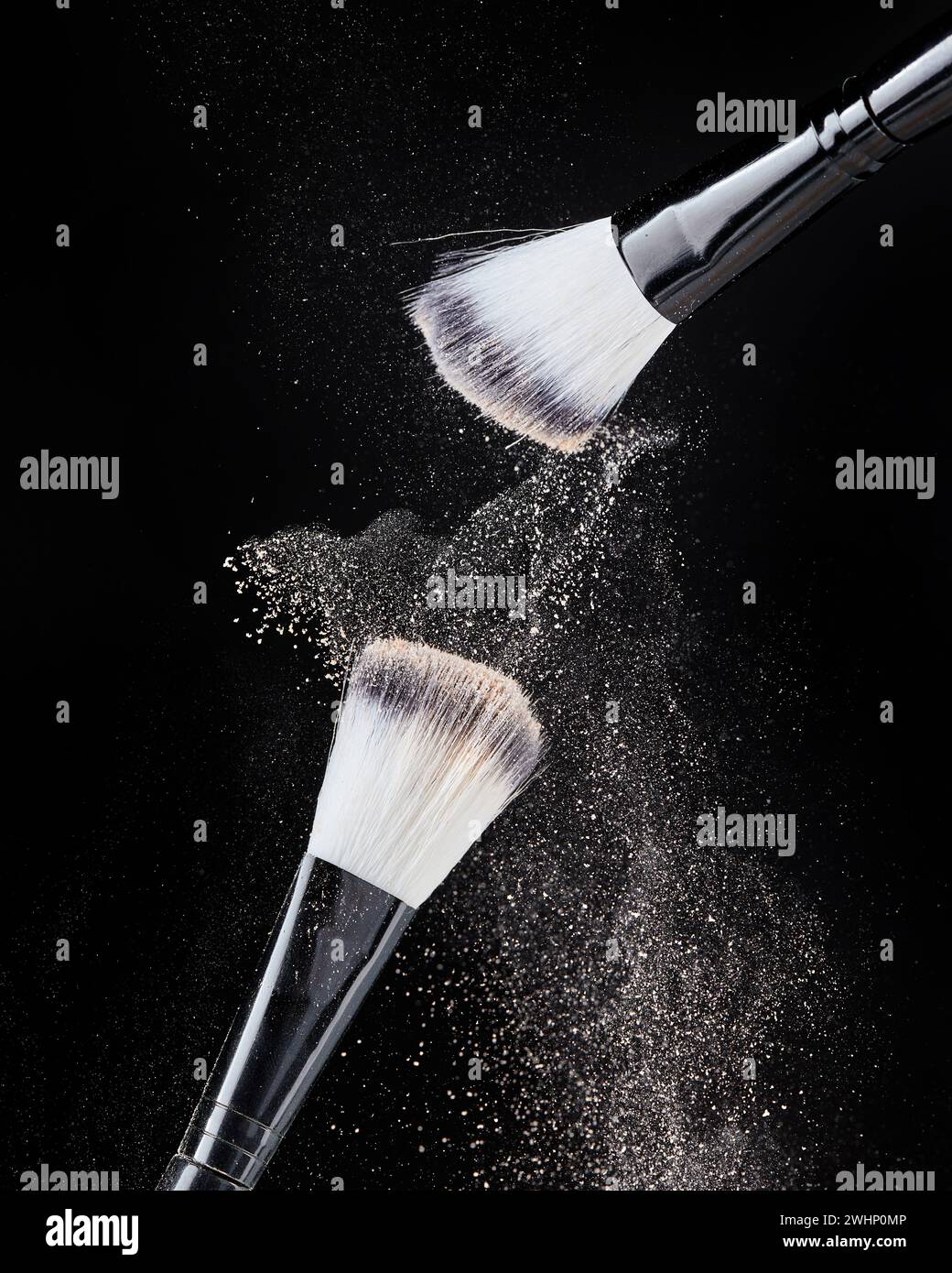 Due spazzole professionali per il trucco nere con polvere beige in movimento e particelle di polvere sparse in forma di clo Foto Stock