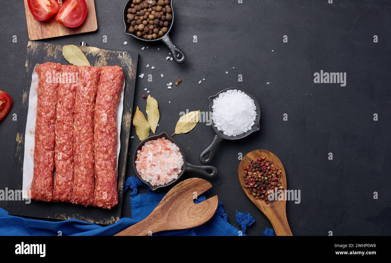 Salsicce crude al kebab di lula su tavola e spezie, vista dall'alto Foto Stock