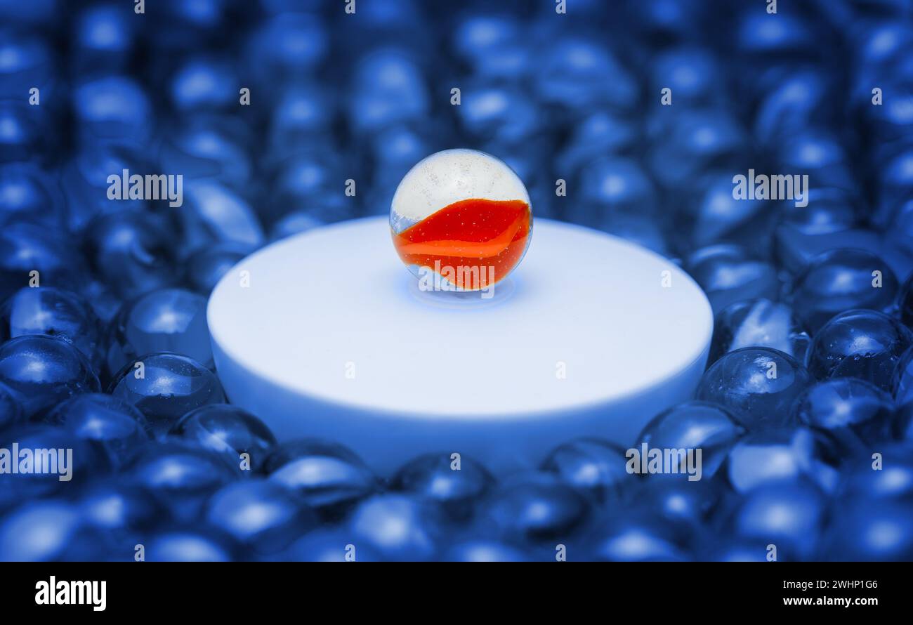 Una sfera di vetro colorata su un podio circondata da semplici sfere di vetro. Macrofotografia con profondità di campo ridotta. Concetto di discorso pubblico, conferenza, Foto Stock