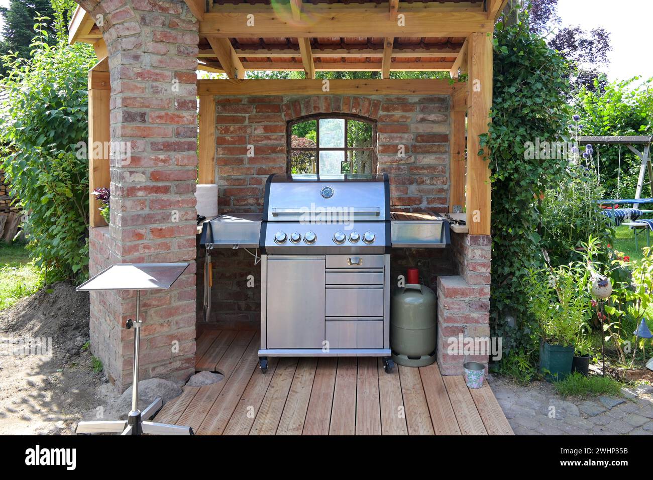 Moderna griglia a gas in acciaio in un riparo fatto di vecchi mattoni e legno, concetto per barbecue e design del giardino Foto Stock