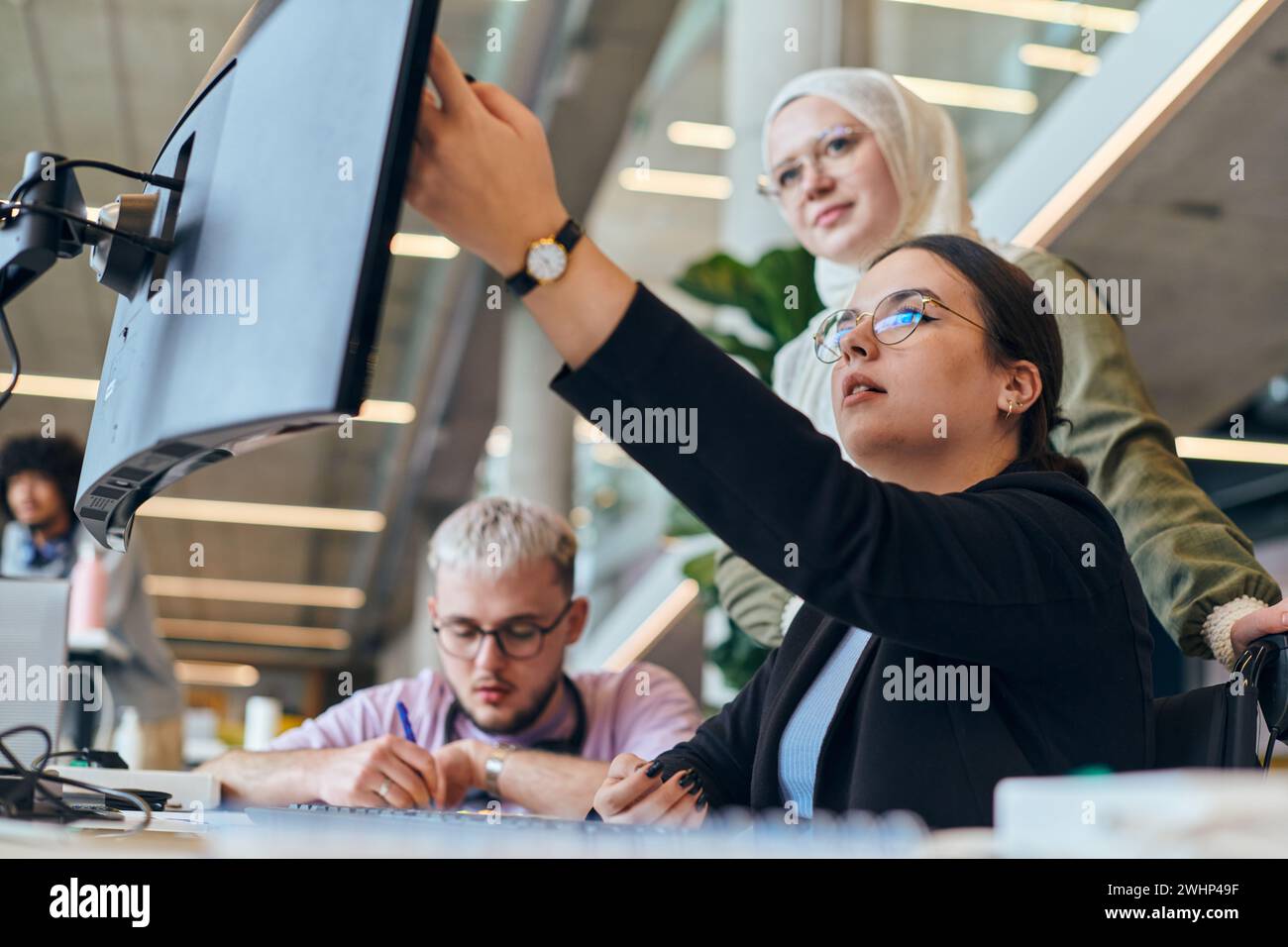 In un moderno ufficio di startup, un gruppo diversificato di giovani professionisti affronta in modo collaborativo vari problemi aziendali e problemi Foto Stock