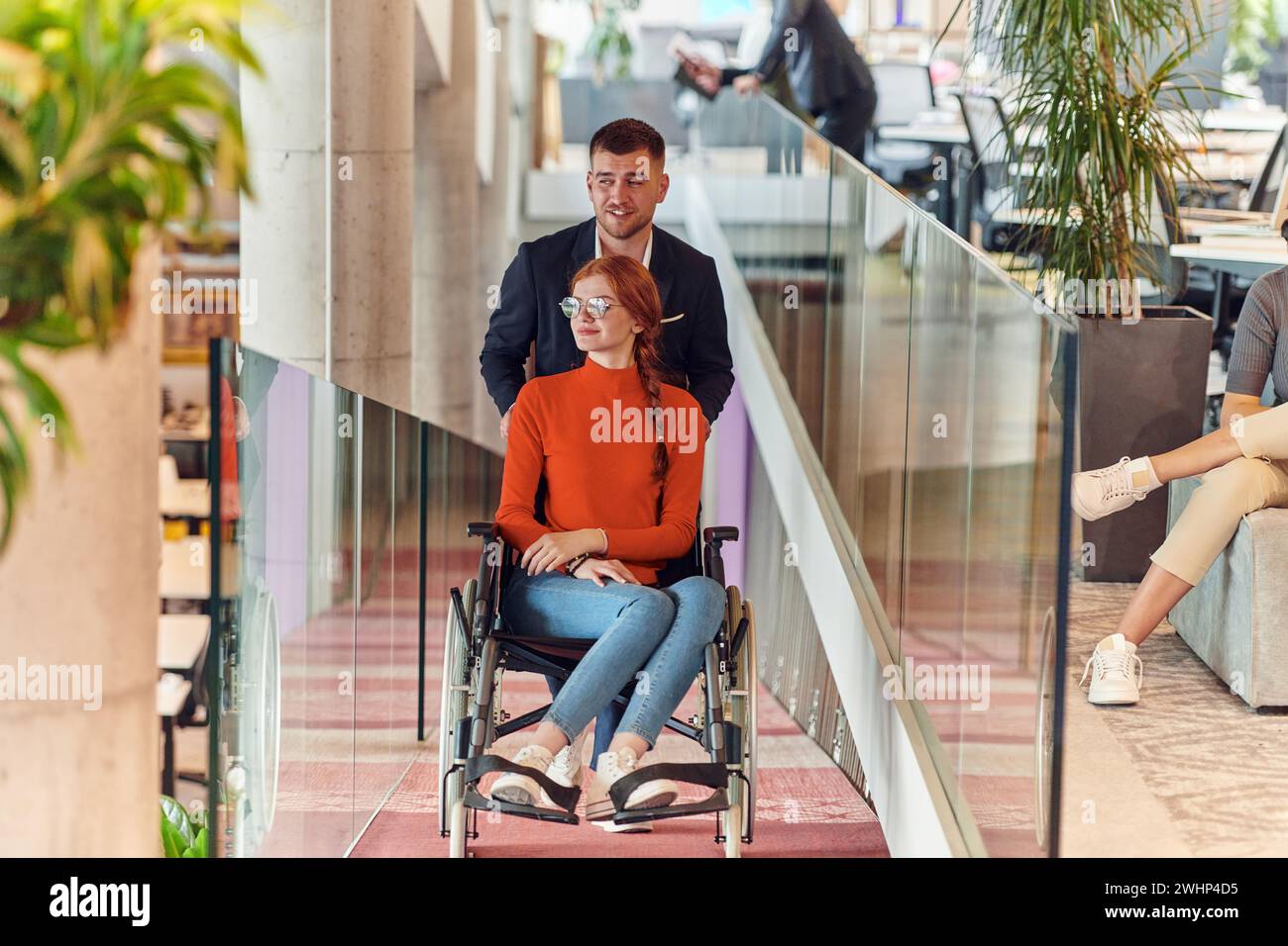 Un direttore dell'azienda assiste il suo collega in sedia a rotelle, aiutandola a raggiungere l'ufficio di startup, dove lavorano Foto Stock