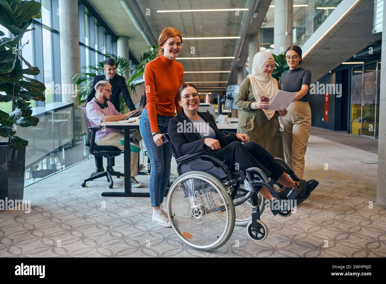 Un gruppo eterogeneo di colleghi d'affari si sta divertendo con il collega che utilizza la sedia a rotelle, dimostrando la loro attenzione e la loro partecipazione Foto Stock