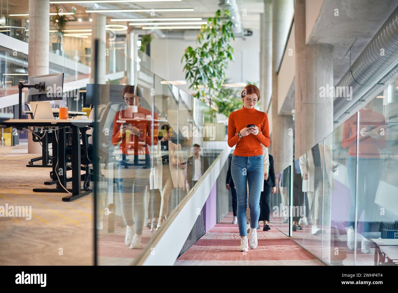 In un vivace e moderno ufficio di startup, una donna d'affari con i capelli arancioni si immerge nel suo lavoro alla sua scrivania, incarnando il Foto Stock