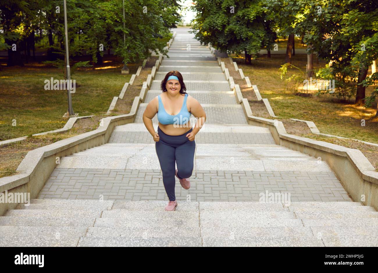 Donna grassa e sorridente in sovrappeso che corre sulle scale del parco estivo della città. Foto Stock