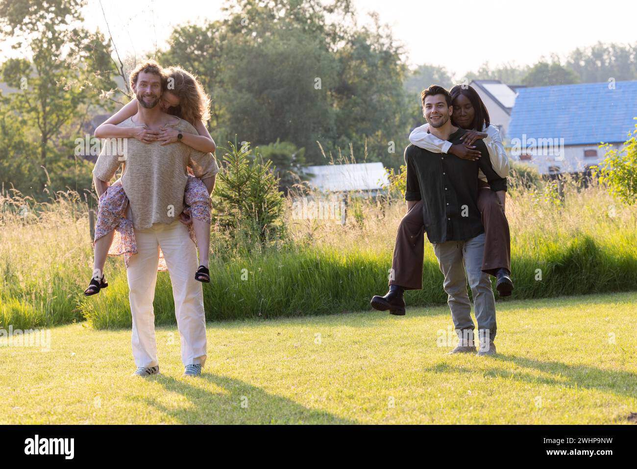 Coppie Millennial gioiose al concorso di equitazione Garden Piggyback Foto Stock