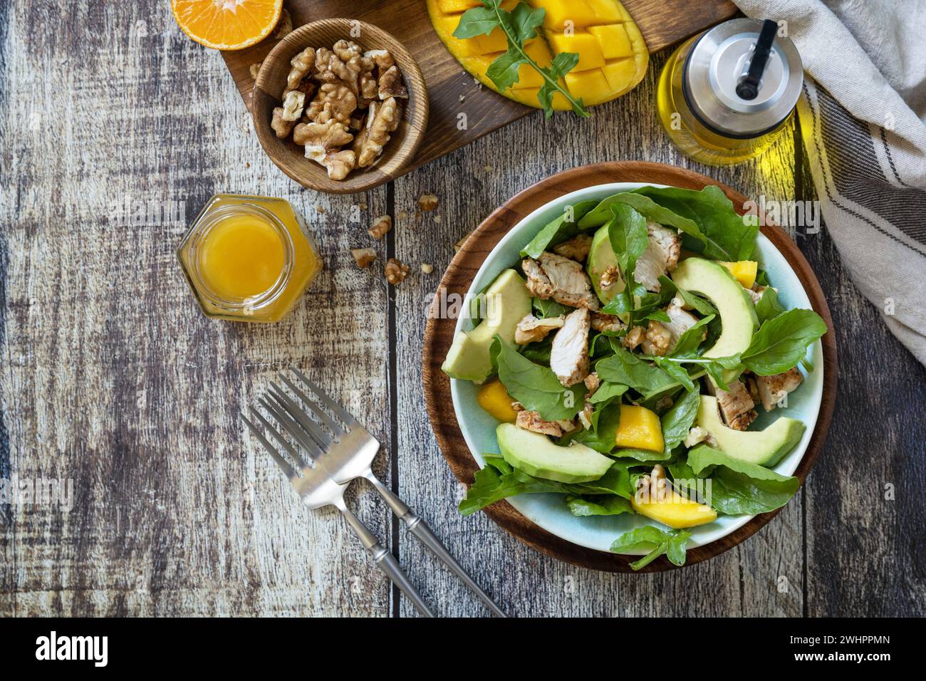 Insalata dietetica sana con pollo, rucola alla griglia, mango, avocado e salsa vinaigrette su un ripiano rustico. Vista dall'alto piatta Foto Stock