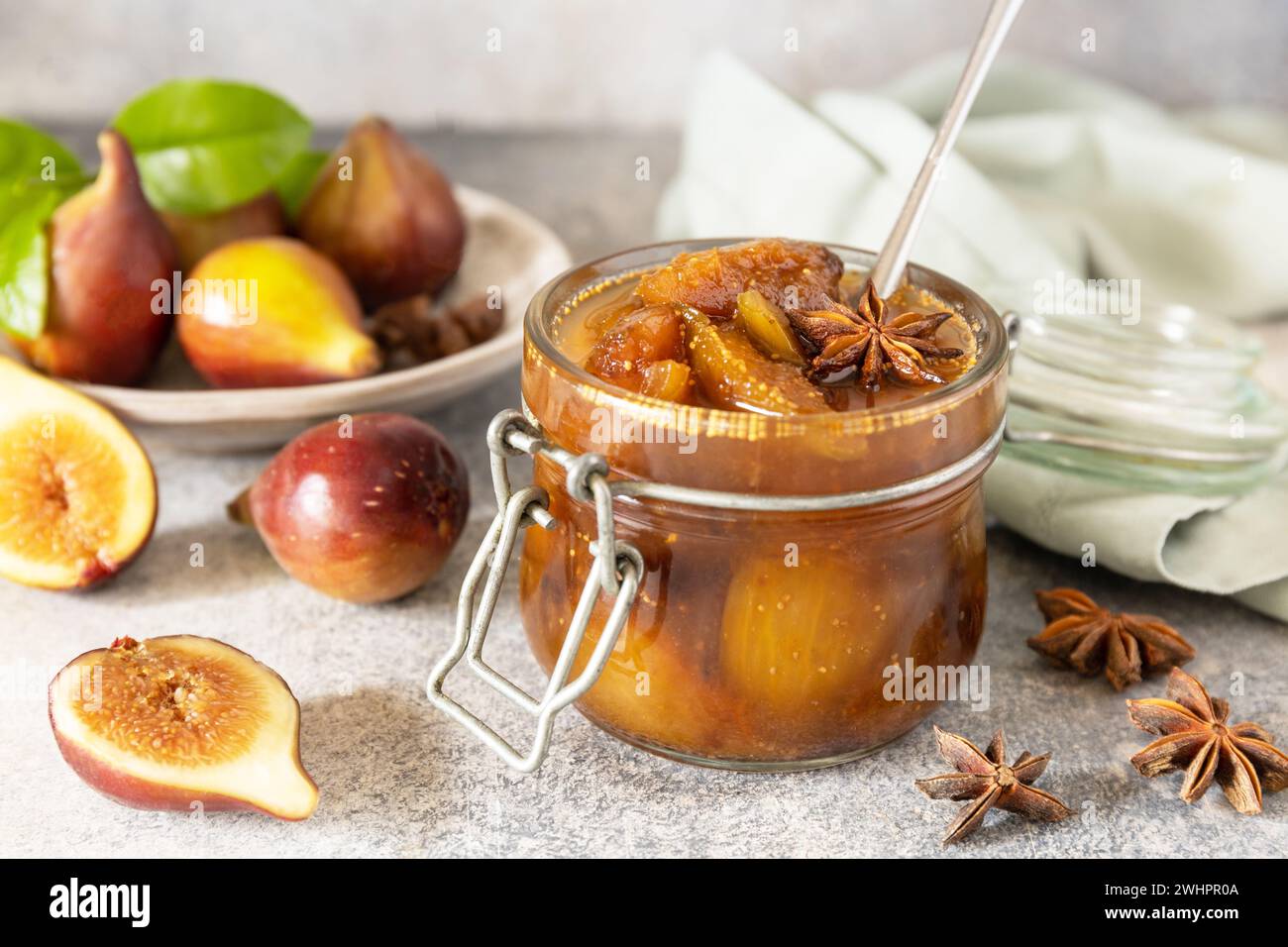 Confettura di fichi fatta in casa in un vaso di vetro con fichi freschi su un tavolo grigio chiaro. Conservazione del raccolto autunnale, cibo fermentato sano Foto Stock