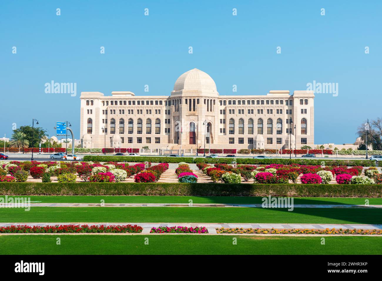 Vista frontale alla Corte Suprema dell'Oman a Mascate, Oman. Giardini assolati in primo piano. Foto Stock